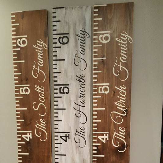 wooden growth charts with measurement markings, personalized with different last names, placed vertically.